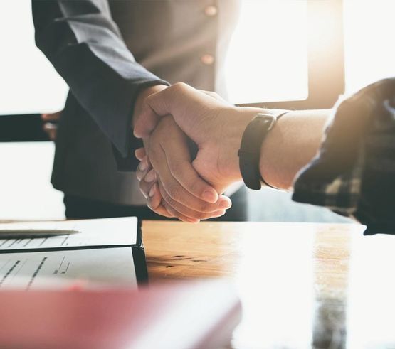 Apretón de manos de negocios sobre un escritorio con papeles bajo una cálida luz de oficina.