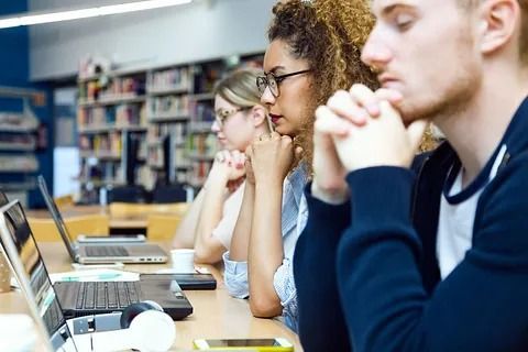 Un grupo de personas está sentado en una mesa con computadoras portátiles en una biblioteca.