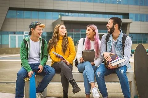 Un grupo de jóvenes está sentado en un banco frente a un edificio.