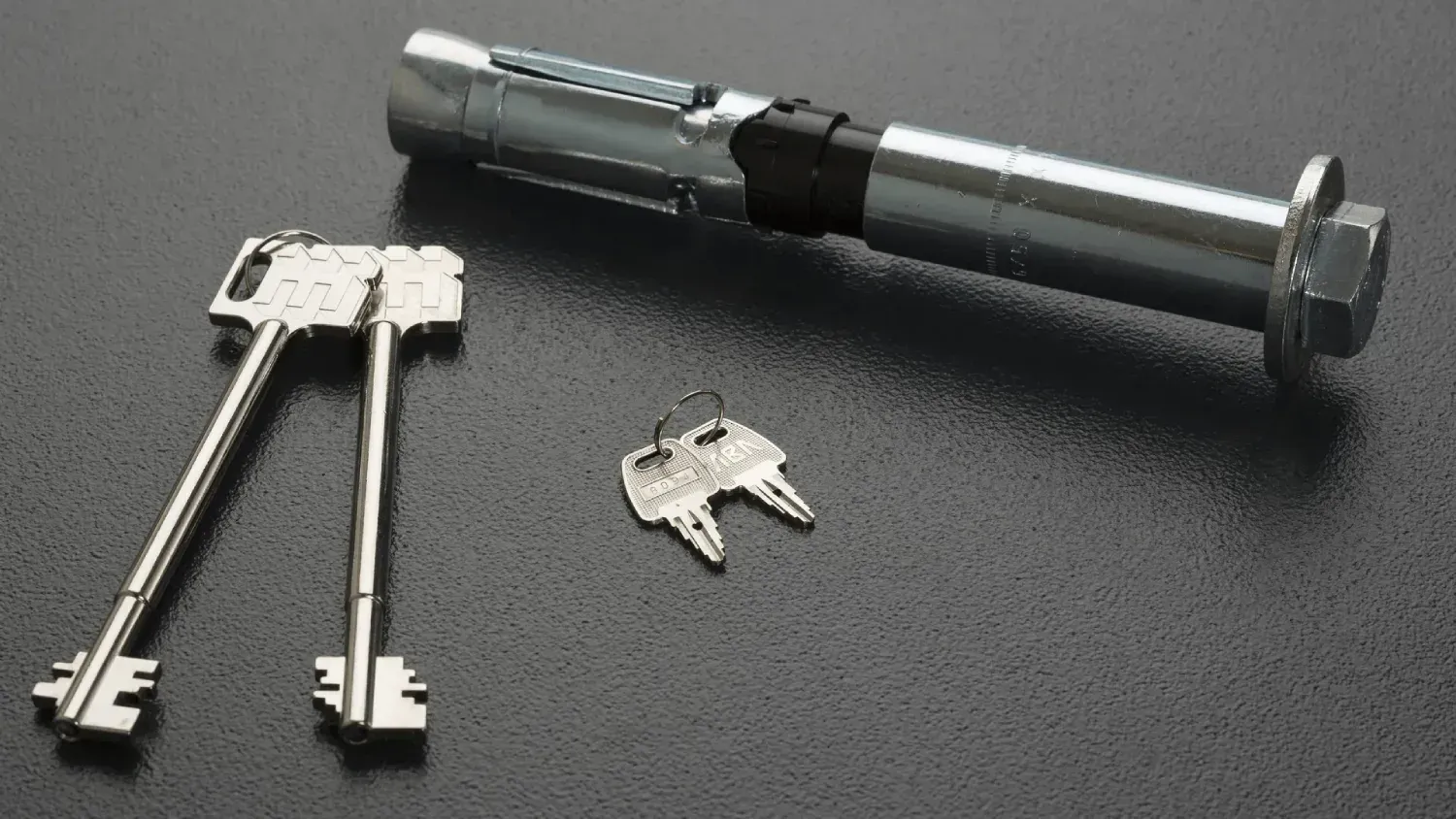 Tres llaves y un cerrojo sobre una superficie oscura.