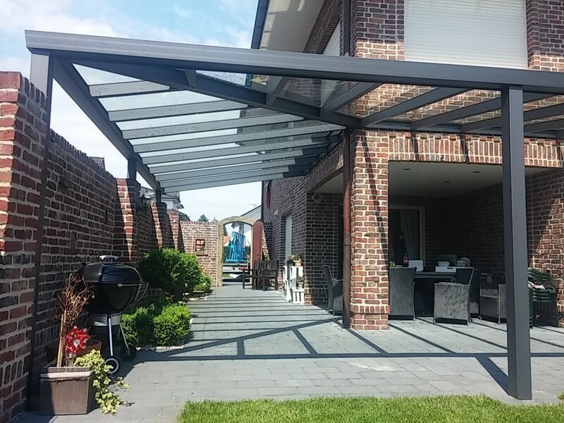 Terrasse mit Backsteinmauern und grauer Markise. Glasdach, Grill und Gartenmöbel sind sichtbar.