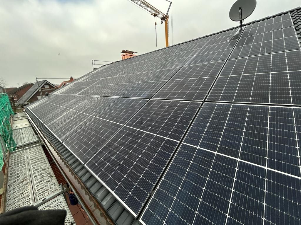 Solarpaneele auf einem Dach, mit einer Satellitenschüssel. Im Hintergrund sind ein Kran und weitere Häuser zu sehen.