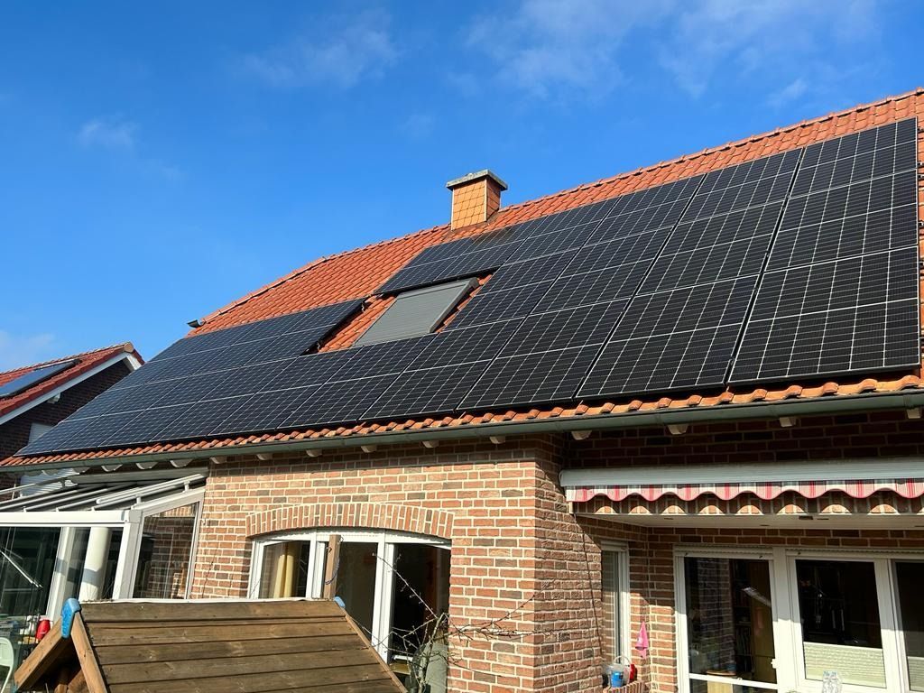Solarpaneele auf dem Dach eines Backsteinhauses unter strahlend blauem Himmel.