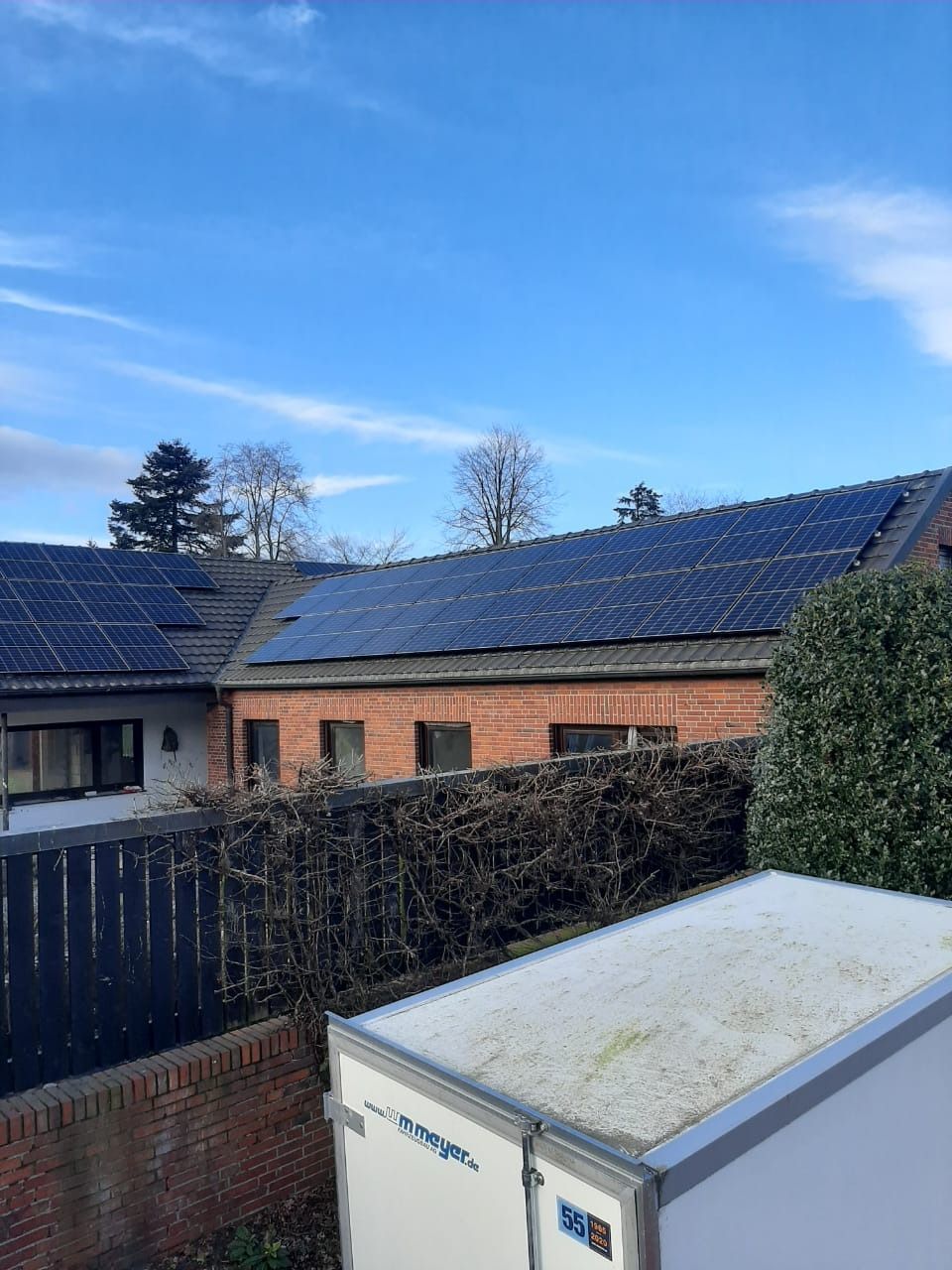 Solarpaneele auf einem Backsteindach vor blauem Himmel, im Vordergrund ein weißer Abstellraum.