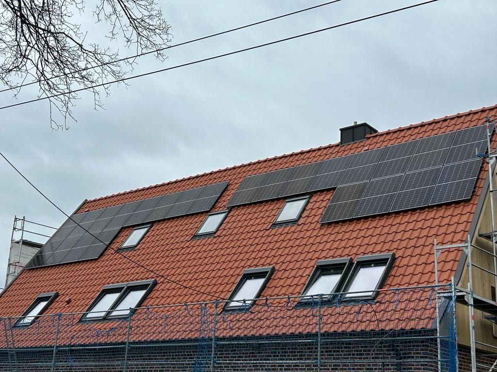Rotes Ziegeldach mit Solarpaneelen und Oberlichtern an einem bewölkten Tag. Blaues Gerüst sichtbar.