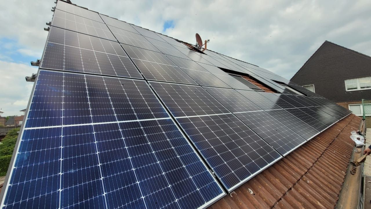 Auf einem Wohnhausdach installierte Solarpaneele spiegeln den bewölkten Himmel wider.