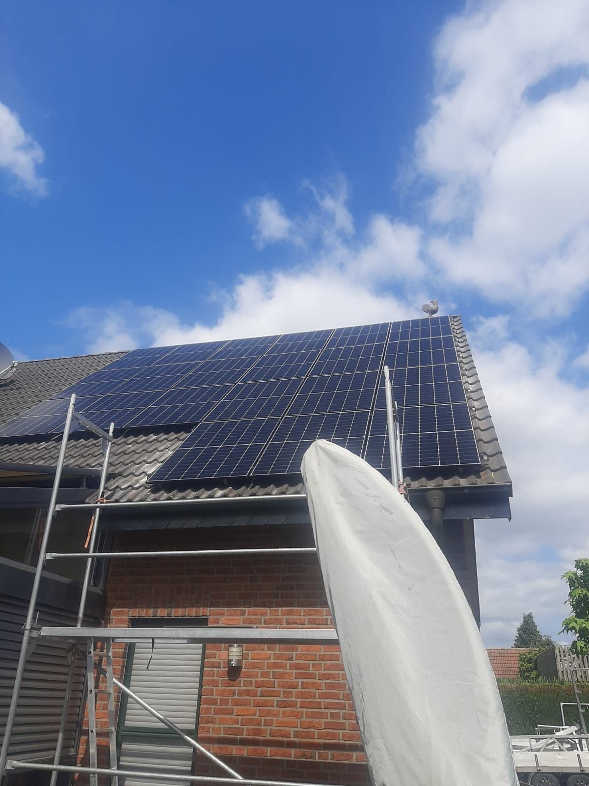 Auf einem Dach installierte Solarpaneele vor blauem Himmel mit Wolken; ein Gerüst ist sichtbar.