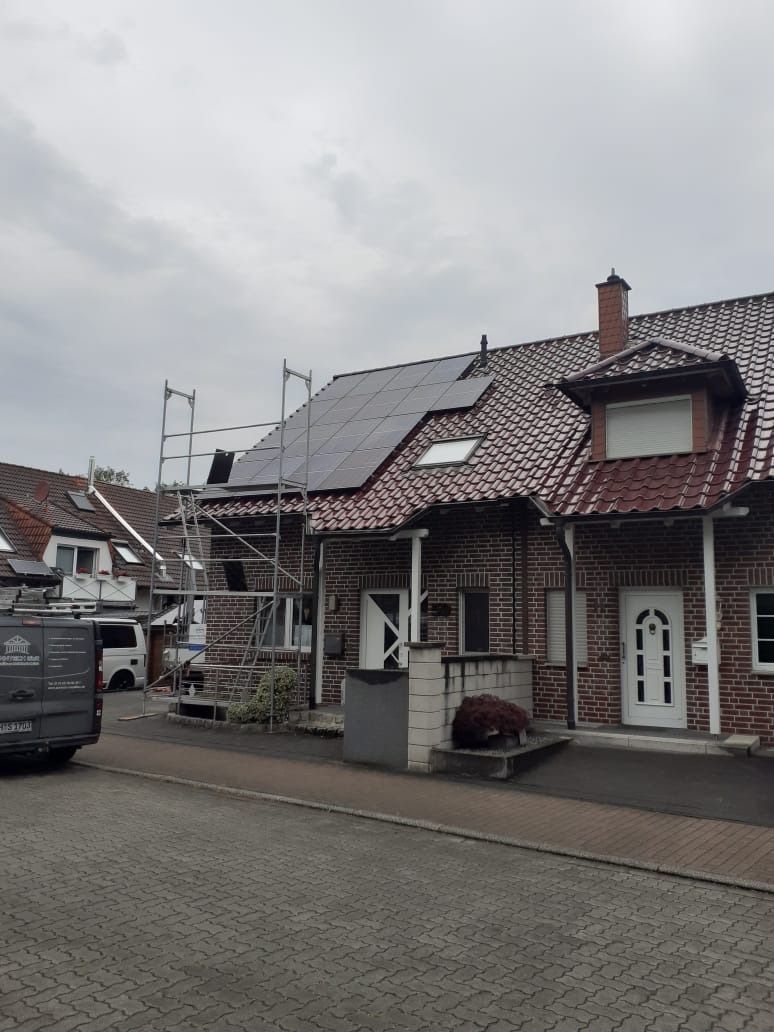Ein Haus mit Solarpaneelen auf dem Dach, einem Baugerüst und einem bewölkten Himmel.