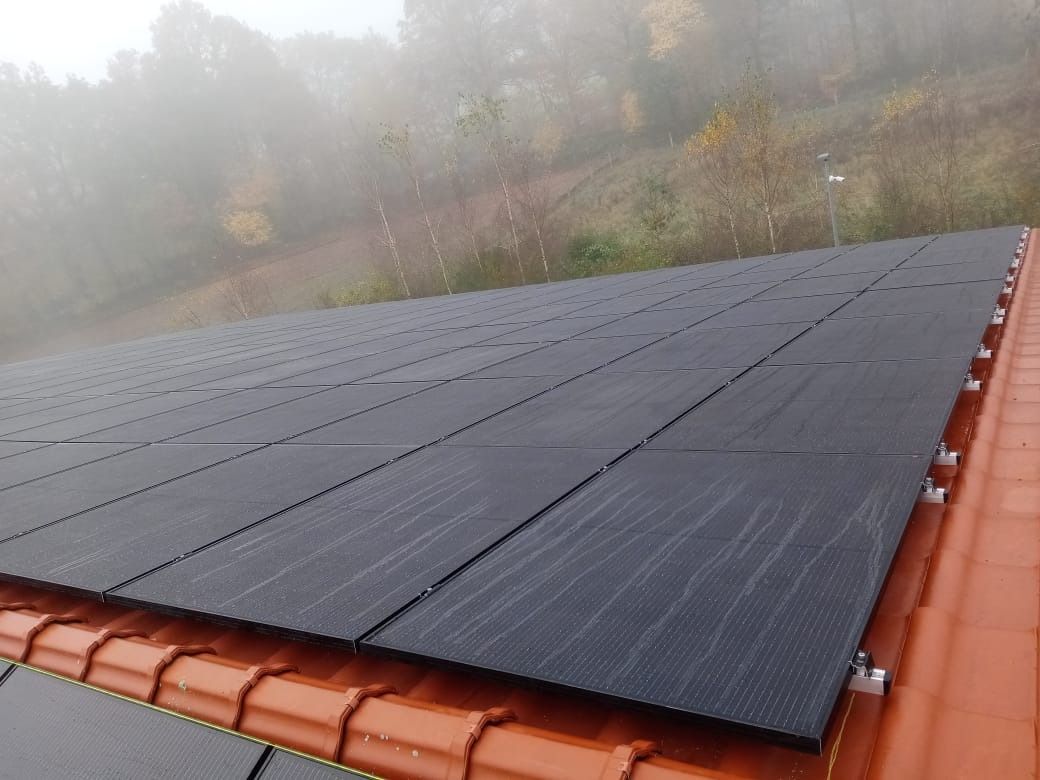 Auf einem mit roten Ziegeln gedeckten Dach installierte Solarpaneele vor der Kulisse eines nebligen, herbstlichen Hügels.