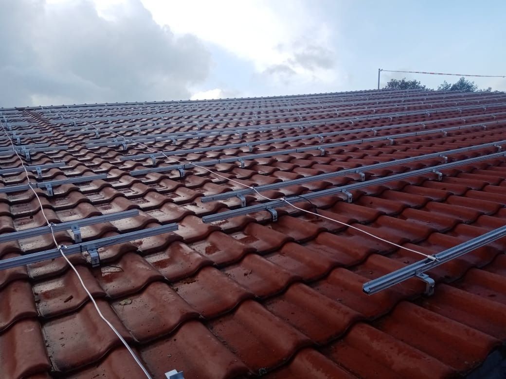 Auf einem roten Ziegeldach werden Solarpaneele mit tragenden Metallrahmen und Verkabelung installiert.