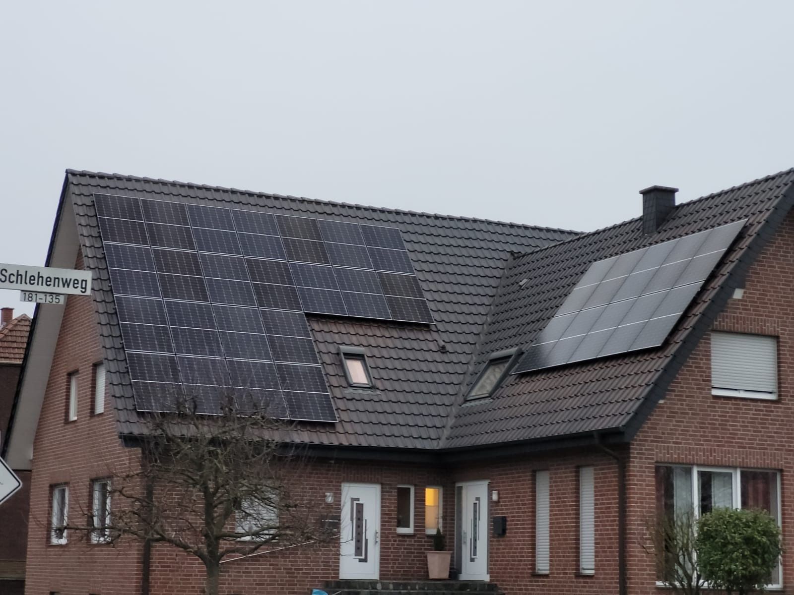 Haus mit Solarpaneelen auf einem dunklen Ziegeldach, Backsteinfassade und einem Straßenschild.