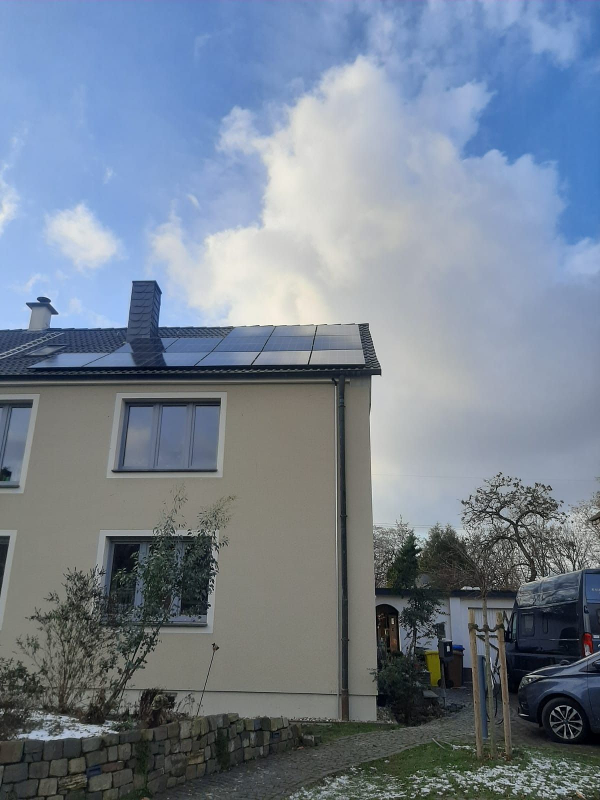 Zweistöckiges Haus mit Solarpaneelen auf dem Dach, bewölkter Himmel.