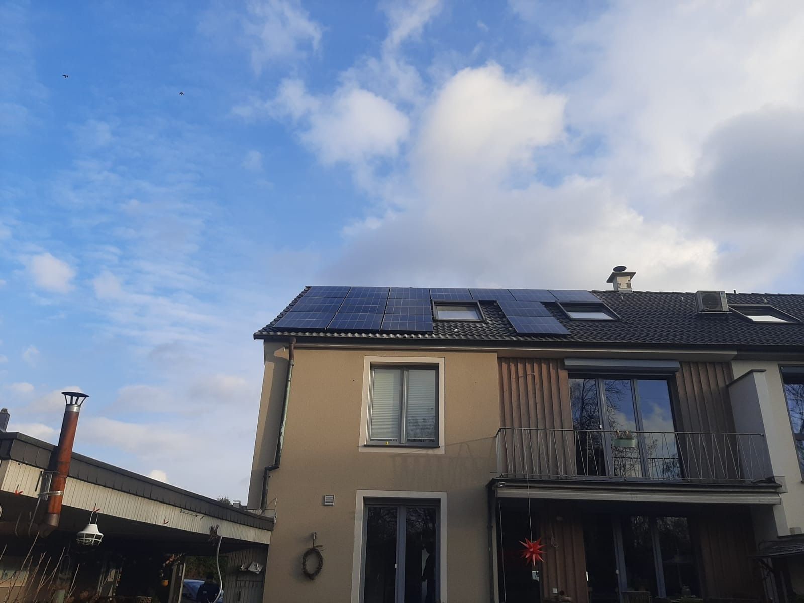 Haus mit Solarpaneelen auf dem Dach unter einem teilweise bewölkten blauen Himmel.