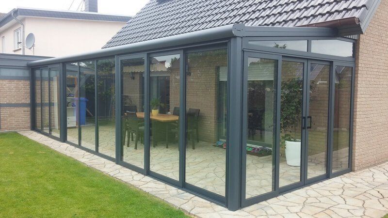 Verglaster Wintergarten, der an ein Backsteinhaus mit gepflasterter Terrasse und Rasenfläche angrenzt.