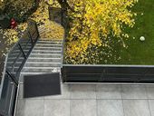 Draufsicht auf eine Außentreppe, die zu einer grünen Rasenfläche mit einem Baum und verstreuten gelben Blättern führt.