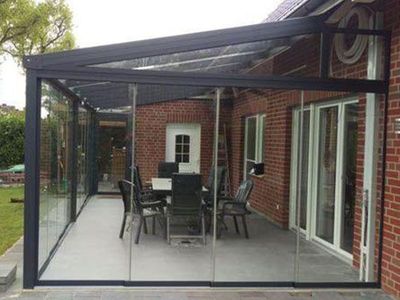 Verglaste Terrasse mit schwarzem Rahmen und Gartenmöbeln neben einem Backsteinhaus.