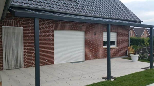 Terrasse mit dunkelgrauer Pergola, Backsteingebäude und weißem Garagentor.