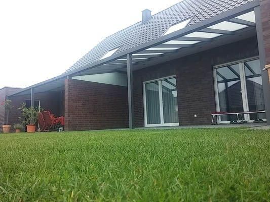 Ein modernes Backsteinhaus mit überdachter Terrasse und grünem Rasen.