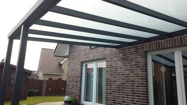 Schwarze Terrassenüberdachung mit weißen Paneelen über einem Backsteinhaus mit großen Fenstern.