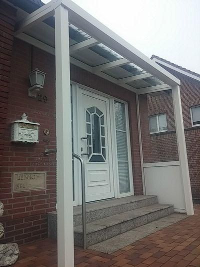 Weiß überdachter Eingangsbereich mit Stufen, die zu einer weißen Tür führen; rotes Backsteingebäude.