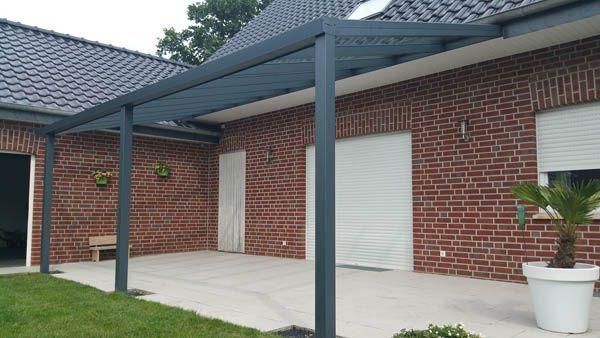 Dunkelgraue Pergola, die an ein Backsteinhaus mit weißer Tür und Fensterläden angebaut ist, über einer Terrasse.