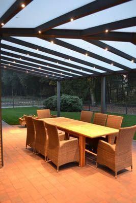 Essbereich im Freien mit Holztisch, Korbstühlen und überdachter Terrasse mit Einbaustrahlern.