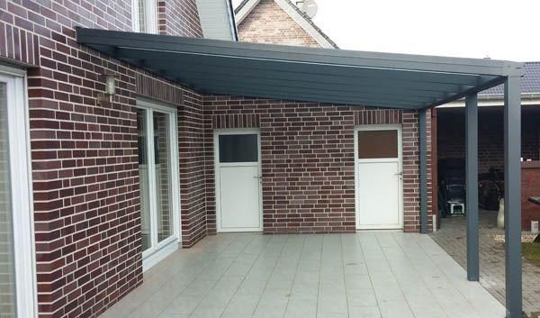 Eine graue Terrassenüberdachung, die an ein Backsteingebäude angebaut ist. Sie hat zwei weiße Türen und eine Glasschiebetür.