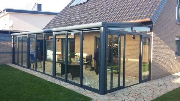 Verglaster Wintergarten an einem Backsteinhaus. Im Vordergrund grüner Rasen und Steinweg.