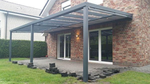 Eine Pergola mit Glastüren ist an ein Backsteinhaus angebaut und steht auf einer Terrasse mit Rasenfläche.