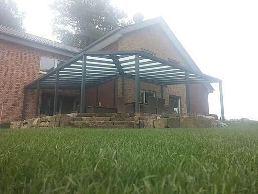 Eine an ein Backsteinhaus angebaute Terrasse mit grauer Markise, die auf einen Rasen überblickt.