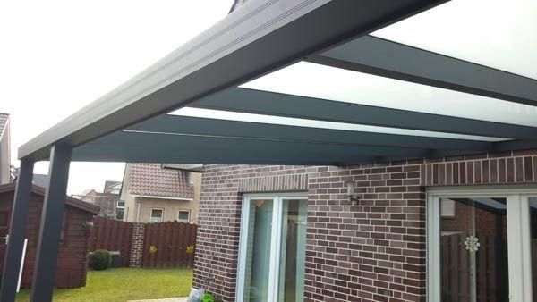 Eine moderne graue Pergola mit lichtdurchlässigen Paneelen, die an ein Backsteinhaus angebaut ist.