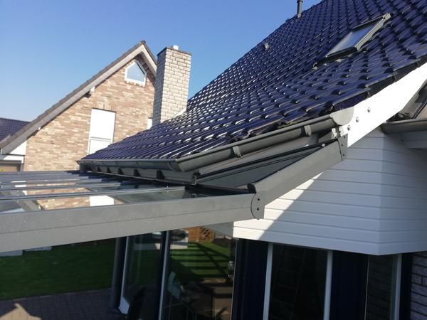 Graues Dach mit Solarpaneelen und einem darüberliegenden Glasdach über einer Außenterrasse.