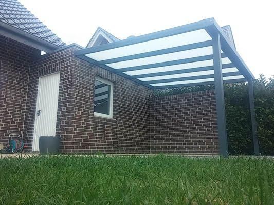 Graue Pergola, die an ein Backsteingebäude über einer Rasenfläche angebaut ist.