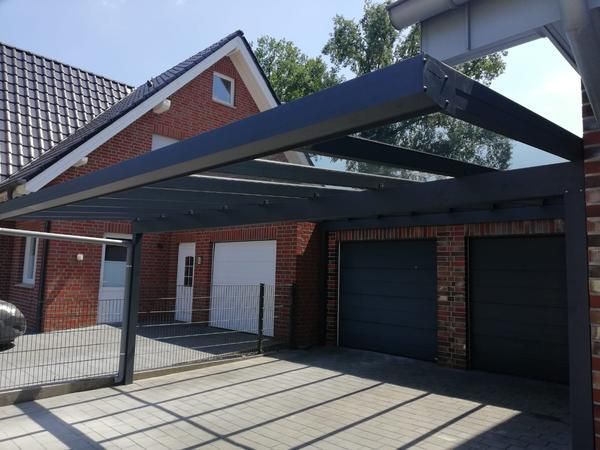 Dunkelgrauer Carport, der an ein Backsteinhaus mit Garage angebaut ist.