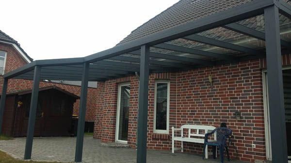 Eine dunkel umrahmte Pergola im Außenbereich ist an ein Backsteinhaus angebaut und überspannt eine Terrasse mit einer weißen Bank.