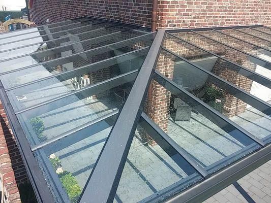 Glasdachkonstruktion mit Metallrahmen auf einem Backsteingebäude.