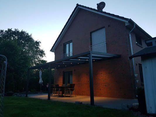 Zweistöckiges Backsteinhaus mit Terrasse und Tisch, das in der Dämmerung beleuchtet wird.