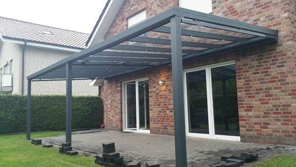 Graue Terrassenmarkise an einem Backsteinhaus über Glasschiebetüren und Terrassenplatten.