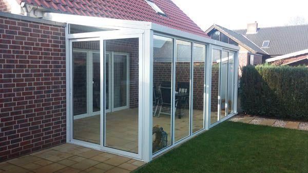 Ein verglaster Wintergarten, der an ein Backsteinhaus angebaut ist und auf einen grünen Rasen blickt.