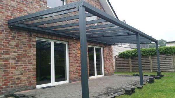 Graue Metall-Terrassenüberdachung, die an einem Backsteingebäude über Glasschiebetüren angebracht ist.