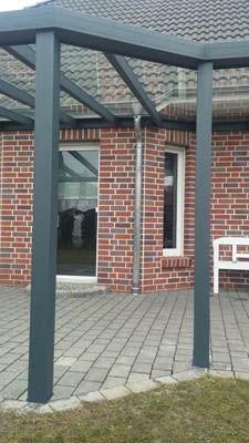 Pergola mit transparentem Dach, getragen von grauen Pfosten, auf einer Ziegelterrasse.