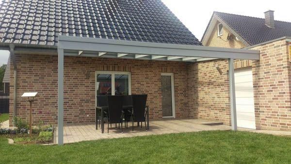 Terrasse mit silbernem Metallrahmendach, Backsteinhaus, Gartentisch und Stühle auf gepflasterter Terrasse.