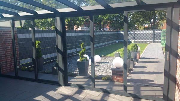 Wintergarten mit schwarzem Rahmen, Glaswänden und Blick auf einen landschaftlich gestalteten Garten.