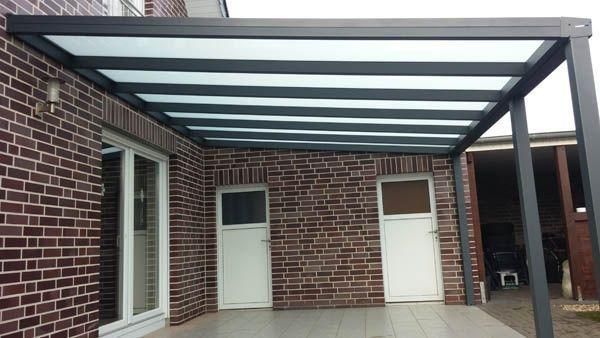 Schwarze Terrassenüberdachung mit Glasdach über einer Backsteinfassade mit weißen Türen und Fenstern.