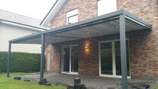 Terrasse mit einer dunkelgrauen Pergola, die an ein Backsteinhaus angebaut ist. Schiebetüren aus Glas sind sichtbar.