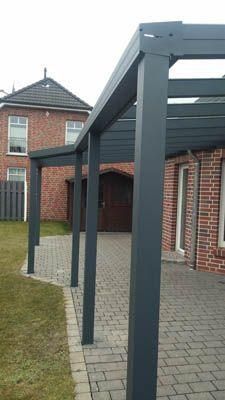 Graue Pergola, die an ein Backsteingebäude angebaut ist, über einer Steinterrasse und Rasen.