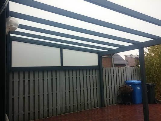 Ein Carport mit grauem Rahmen und lichtdurchlässigem Dach, der an einen Holzzaun angebaut ist.