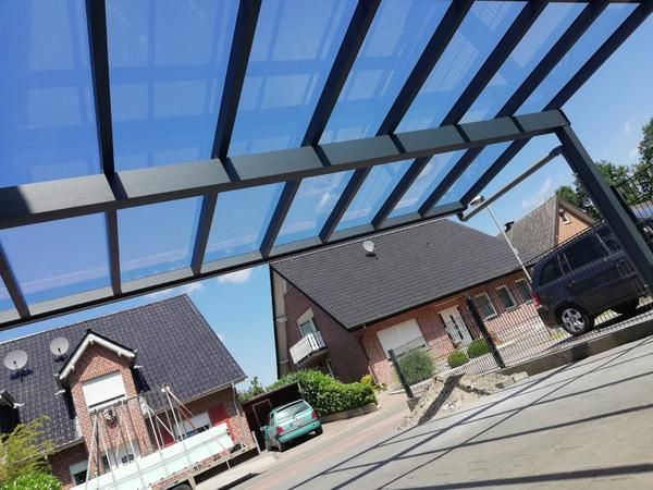 Moderner Carport mit transparenten Dachpaneelen, vor Häusern unter sonnigem, blauem Himmel.