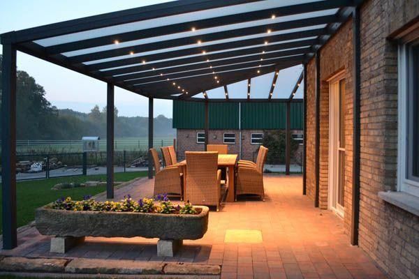 Terrasse mit Essbereich unter einer überdachten und beleuchteten Konstruktion neben einem Backsteingebäude.