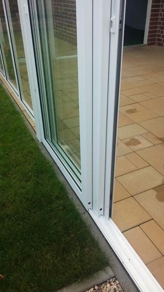 Weiße Glasschiebetüren auf einer Terrasse mit sichtbarer Backsteinmauer.